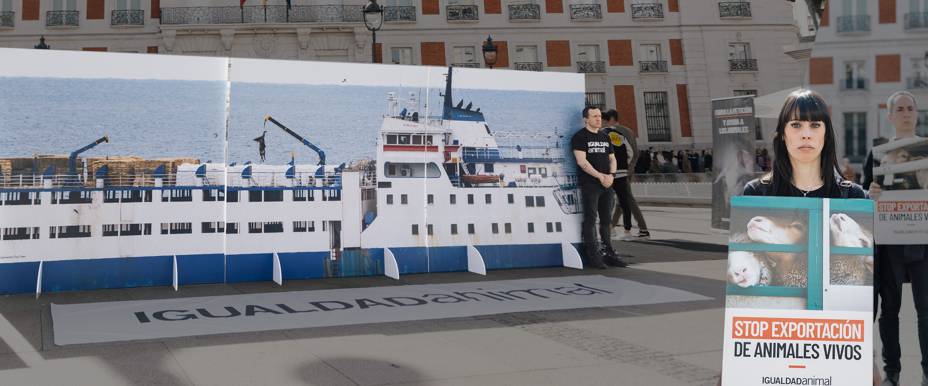 Fotografía de la Puerta del Sol de Madrid con una répicla de un buque que transporta animales vivos. Activista sujetando cartel a un lado. Con degradado en oscuro.